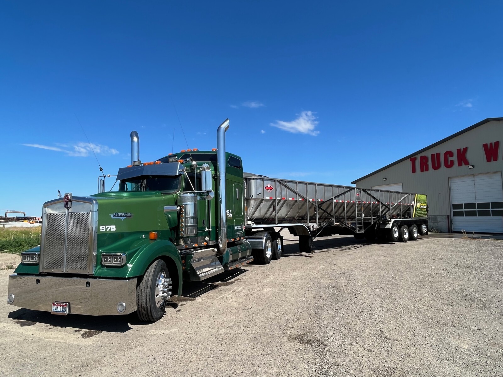 Green Peterbilt with belt trailer infront of Truck Wash building